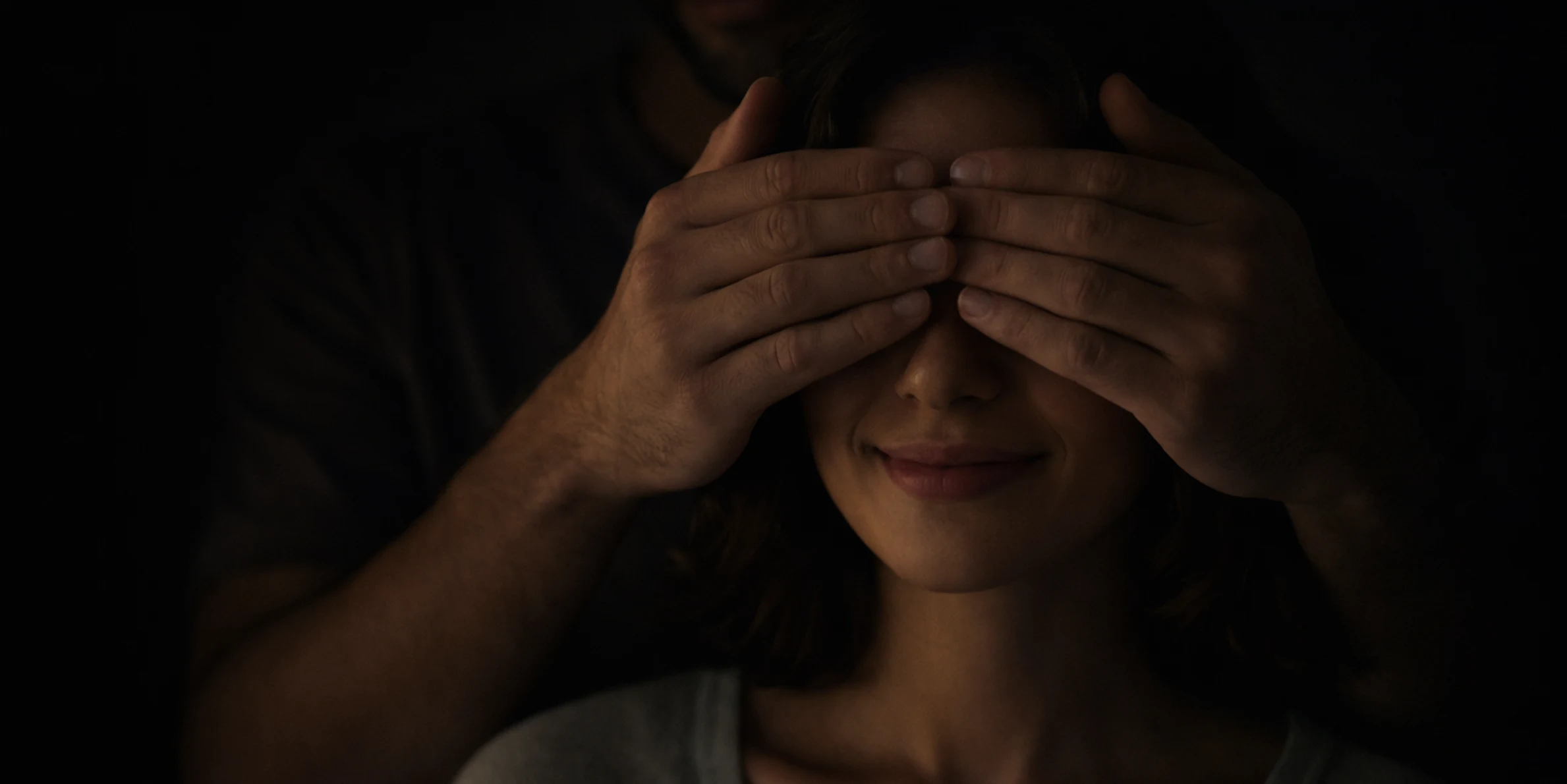 Partner covering woman's eyes playfully in dim bedroom setting